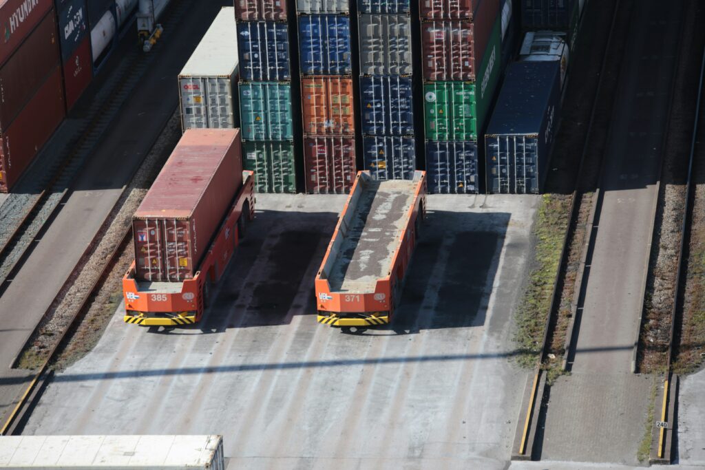 Two orange cargo containers parked beside stacked shipping containers at a freight yard.